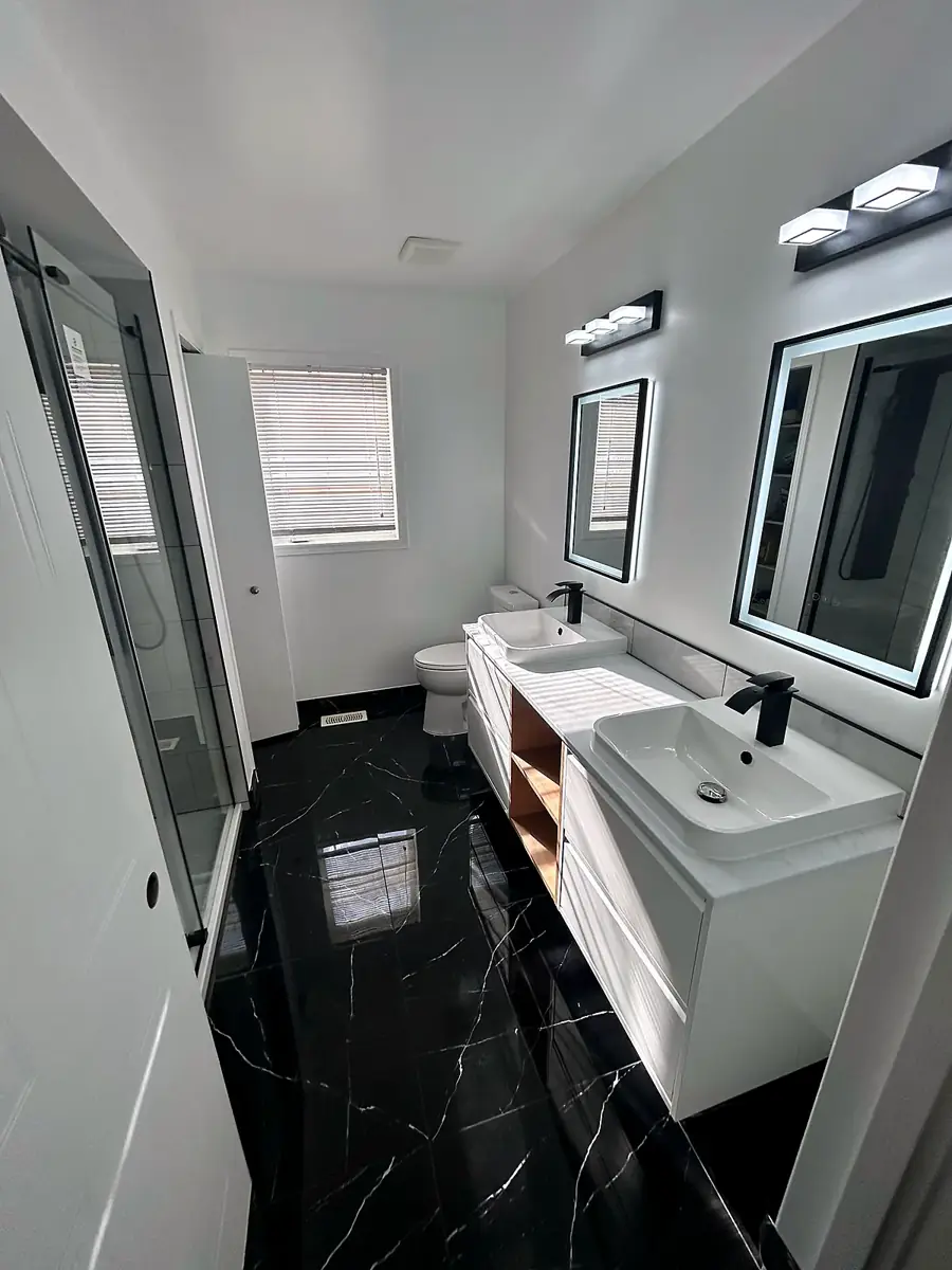 Long bathroom with double vanity and glass shower